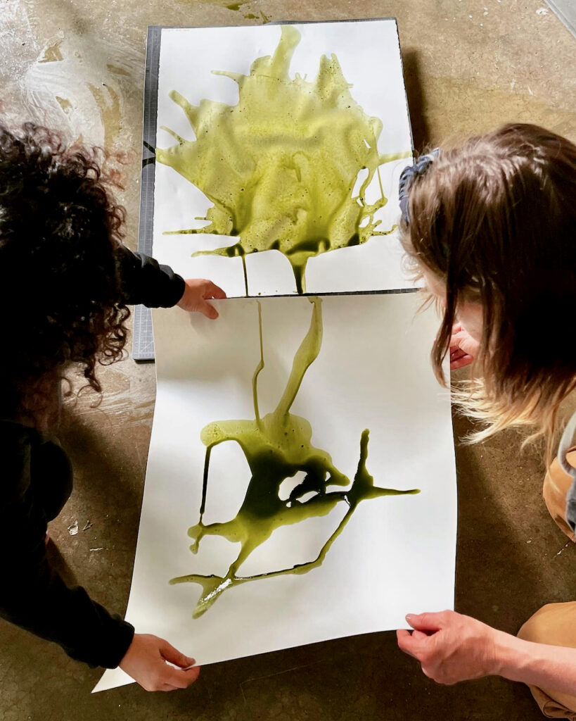 two people pouring chard emulsion onto two sheets of paper